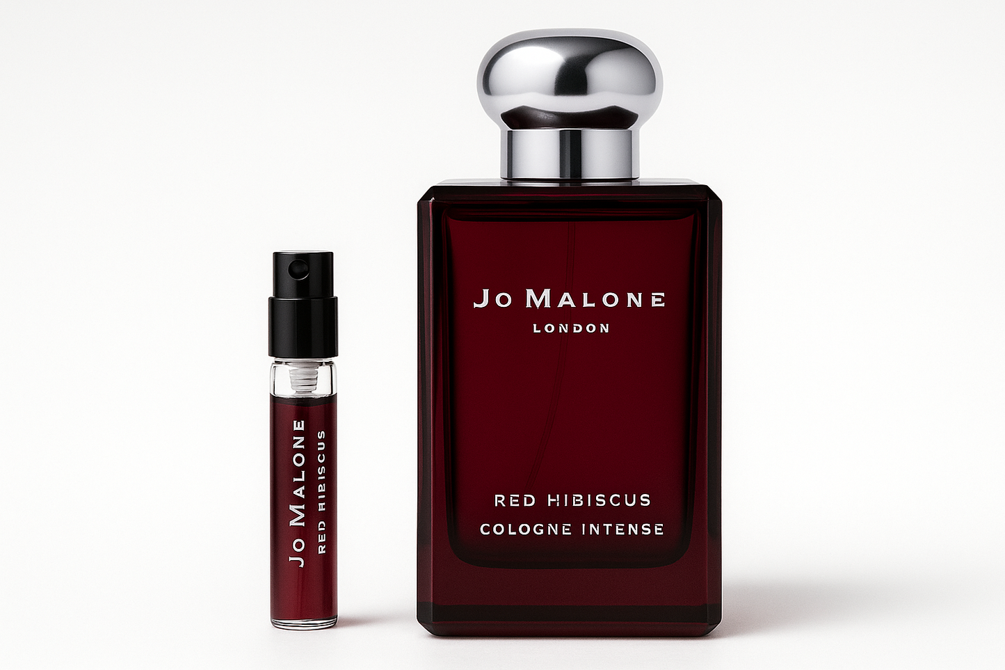 Próbka wody kolońskiej Jo Malone Red Hibiscus Intense 2 ml stojąca obok 100 ml butelki perfum Jo Malone Red Hibiscus Intense z białym napisem na ciemnoczerwonej butelce