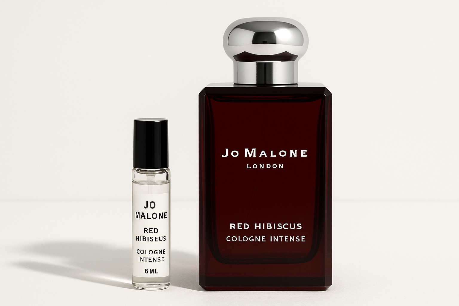 Próbka wody kolońskiej Jo Malone Red Hibiscus Intense 6 ml stojąca obok 100-mililitrowej butelki perfum Jo Malone Red Hibiscus Intense z białym napisem na ciemnoczerwonej butelce